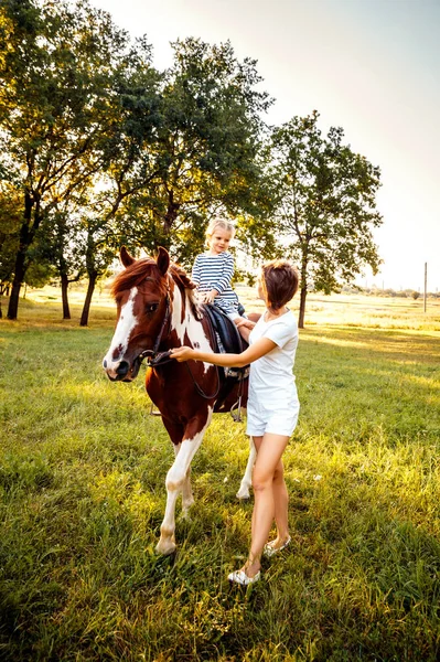 Menina montando em um cavalo com sua mãe andando nas proximidades — Fotografia de Stock