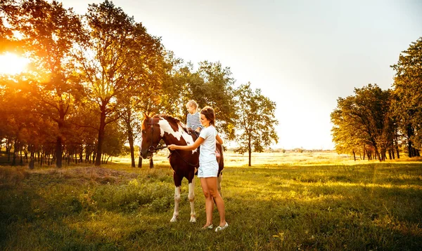Niña montando a caballo con su madre de pie cerca — Foto de Stock