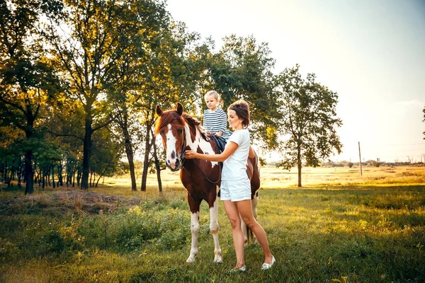 Menina montando em um cavalo com sua mãe de pé nearb — Fotografia de Stock