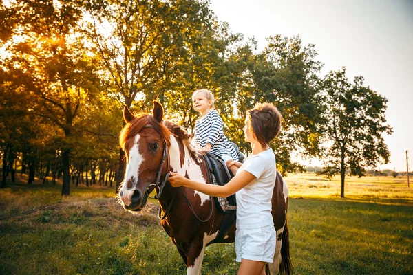 Маленькая девочка едет верхом на лошади со своей матерью, идущей рядом — стоковое фото
