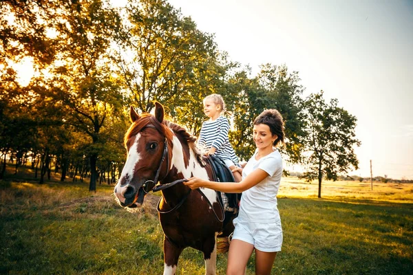 Menina montando em um cavalo com sua mãe andando nas proximidades — Fotografia de Stock