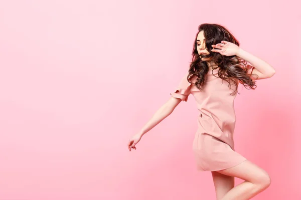 스튜디오 핑크 배경에서 분홍색 드레스에 긴 곱슬 머리를 가진 아름 다운 유행 소녀. — 스톡 사진