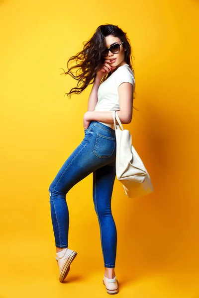 Hermosa joven en gafas de sol, camisa blanca, vaqueros azules posando con bolsa — Foto de Stock