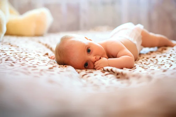 Bébé fille heureuse portant des pantoufles dans une chambre blanche ensoleillée couchée sur un lit blanc. Nouveau-né relaxant au lit après le bain ou la douche. Concept enfant nouveau-né . — Photo