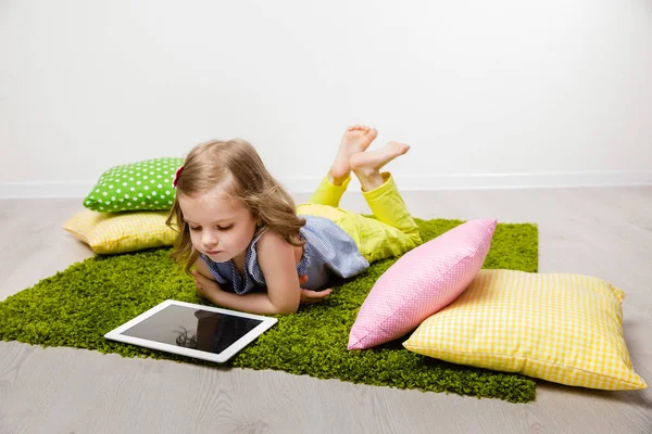The little girl lies on a rug, watches the tablet. — Stock Photo, Image