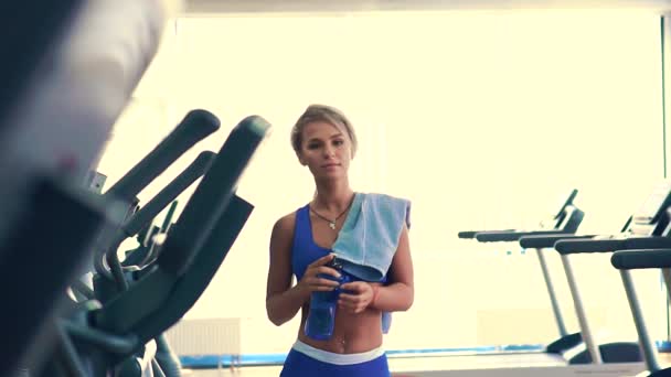 Sportwoman está bebiendo agua de la botella de plástico azul después del entrenamiento duro — Vídeo de stock
