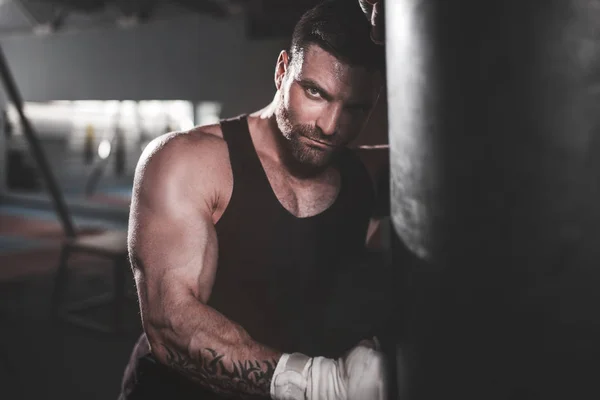 Male boxer training with punching bag in dark sports hall. — Stock Photo, Image