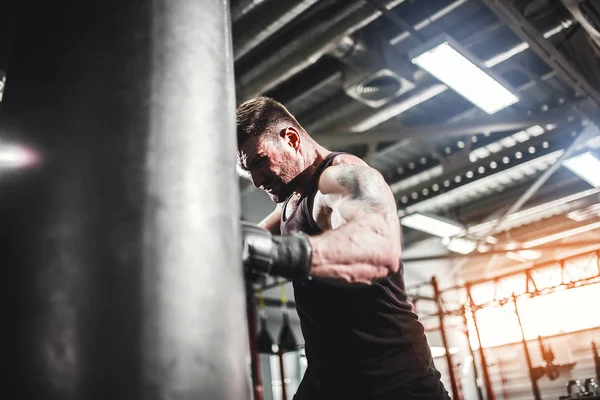 Male boxer training with punching bag in dark sports hall.