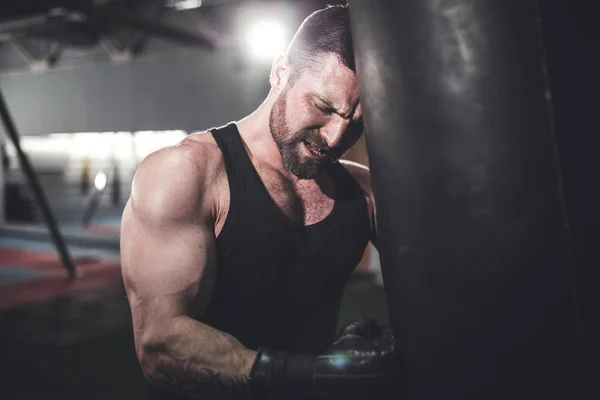 Male boxer training with punching bag in dark sports hall.