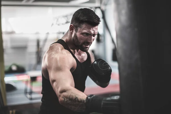 Entrenamiento de boxeador masculino con saco de boxeo en pabellón deportivo oscuro. —  Fotos de Stock