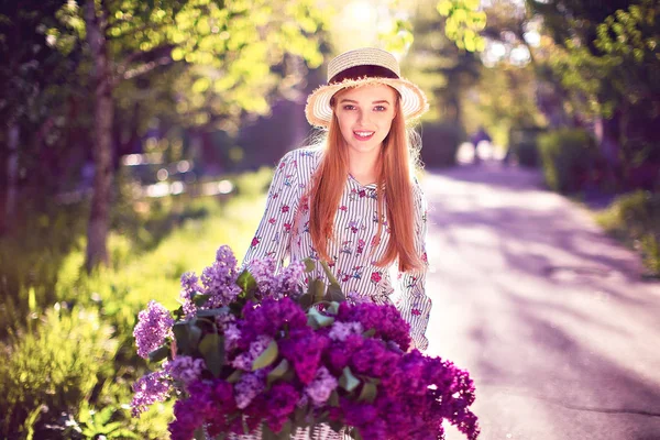 Mooi jong meisje met vintage fiets en bloemen op stad achtergrond in het zonlicht buiten. — Stockfoto