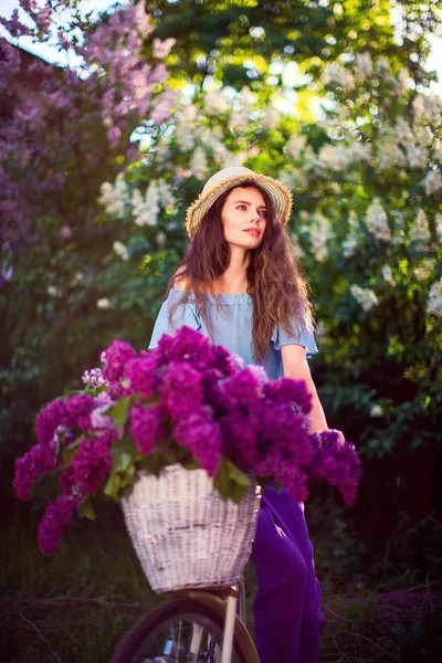 Bella ragazza con bicicletta vintage e fiori sullo sfondo della città alla luce del sole all'aperto . — Foto Stock