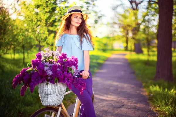 Bella ragazza con bicicletta vintage e fiori sullo sfondo della città alla luce del sole all'aperto . — Foto Stock