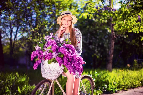 Hermosa joven con bicicleta vintage y flores en el fondo de la ciudad a la luz del sol al aire libre . — Foto de Stock