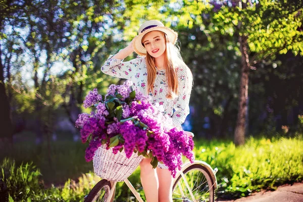 Hermosa joven con bicicleta vintage y flores en el fondo de la ciudad a la luz del sol al aire libre . —  Fotos de Stock