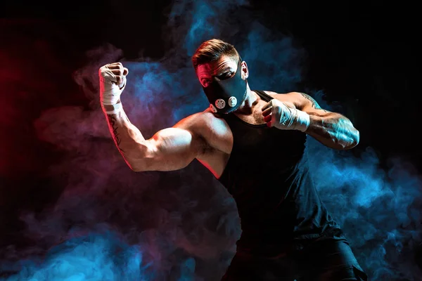 Strong male athlete in a black training mask on a black background — Stock Photo, Image