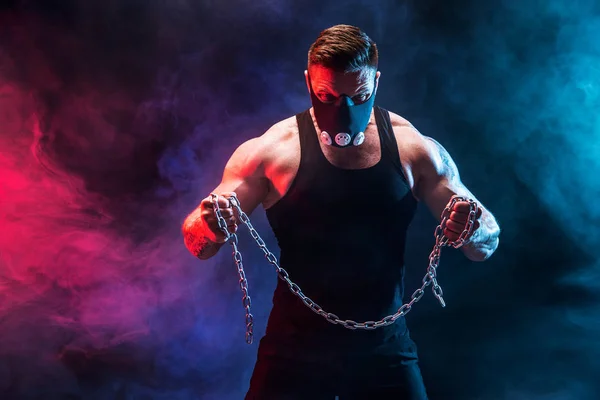 Portret van gespierde sportman scheuren metalen ketting. Zwarte achtergrond met rook — Stockfoto