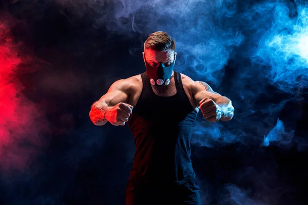 Strong male athlete in a black training mask on a black background — Stock Photo, Image