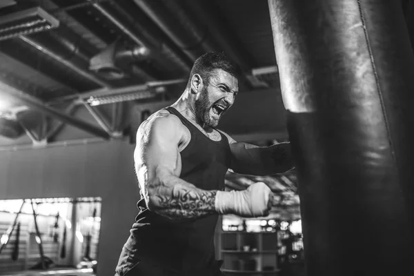 Treinamento boxeador masculino com saco de perfuração no salão de esportes escuro. — Fotografia de Stock