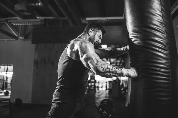 Treinamento boxeador masculino com saco de perfuração no salão de esportes escuro. — Fotografia de Stock