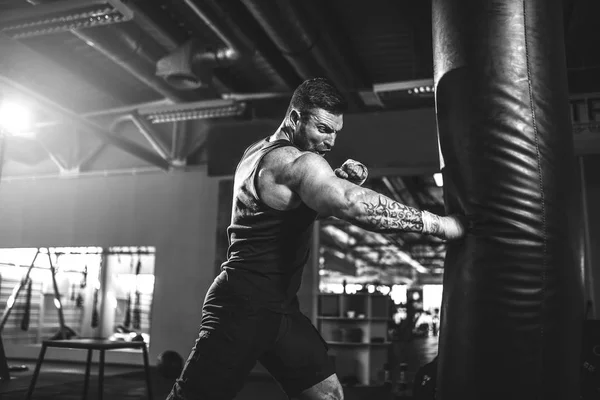 Male boxer training with punching bag in dark sports hall.