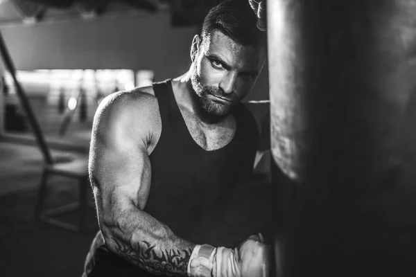 Male boxer training with punching bag in dark sports hall. — Stock Photo, Image