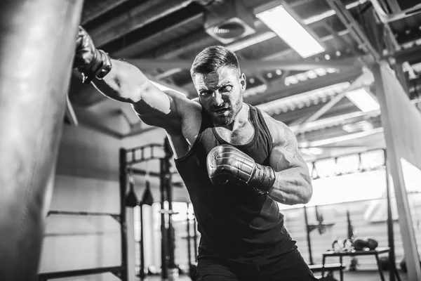 Mužský boxer trénink s boxovací taškou v tmavé sportovní hale. — Stock fotografie
