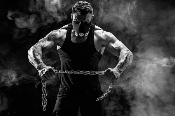 Retrato de deportista musculoso desgarrando cadena metálica. Fondo negro con humo — Foto de Stock