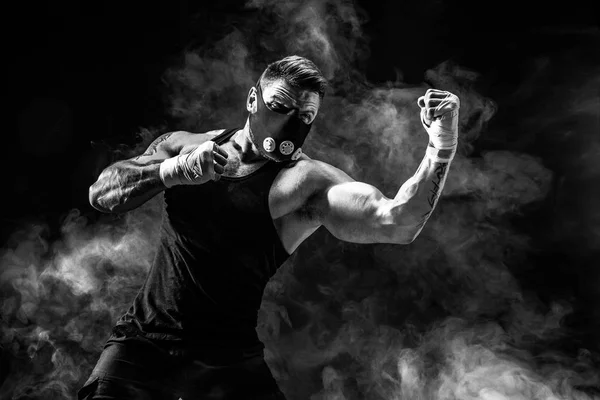 Strong male athlete in a black training mask on a black background — Stock Photo, Image