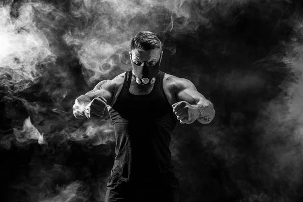 Strong male athlete in a black training mask on a black background — Stock Photo, Image