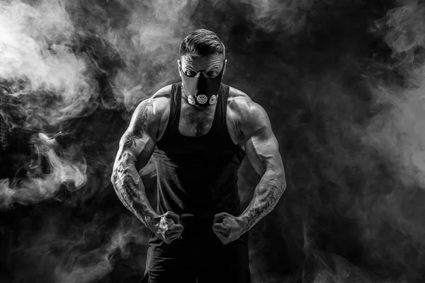 Atleta masculino forte em uma máscara de treinamento preto em um fundo preto — Fotografia de Stock