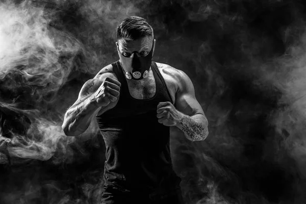 Forte atleta maschio in una maschera di allenamento nero su uno sfondo nero — Foto Stock
