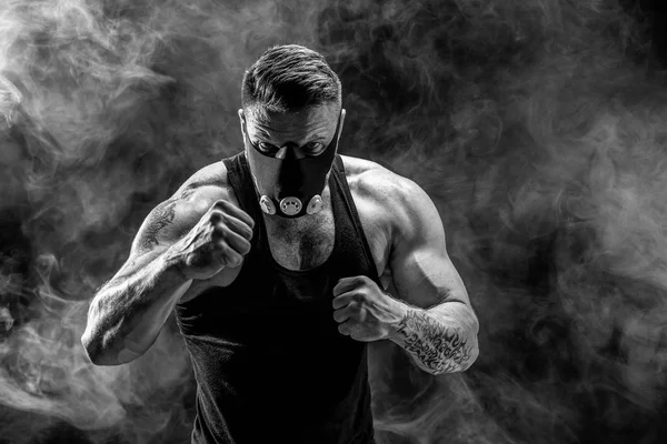 Forte atleta maschio in una maschera di allenamento nero su uno sfondo nero — Foto Stock