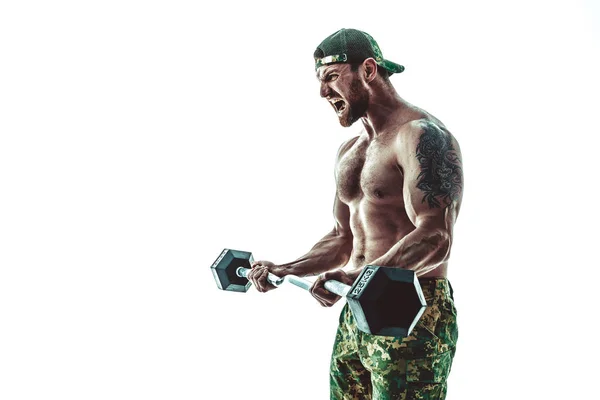 Muskulös idrottare bodybuilder man i camouflage byxor med en naken bål träning med hantel på en vit bakgrund. — Stockfoto