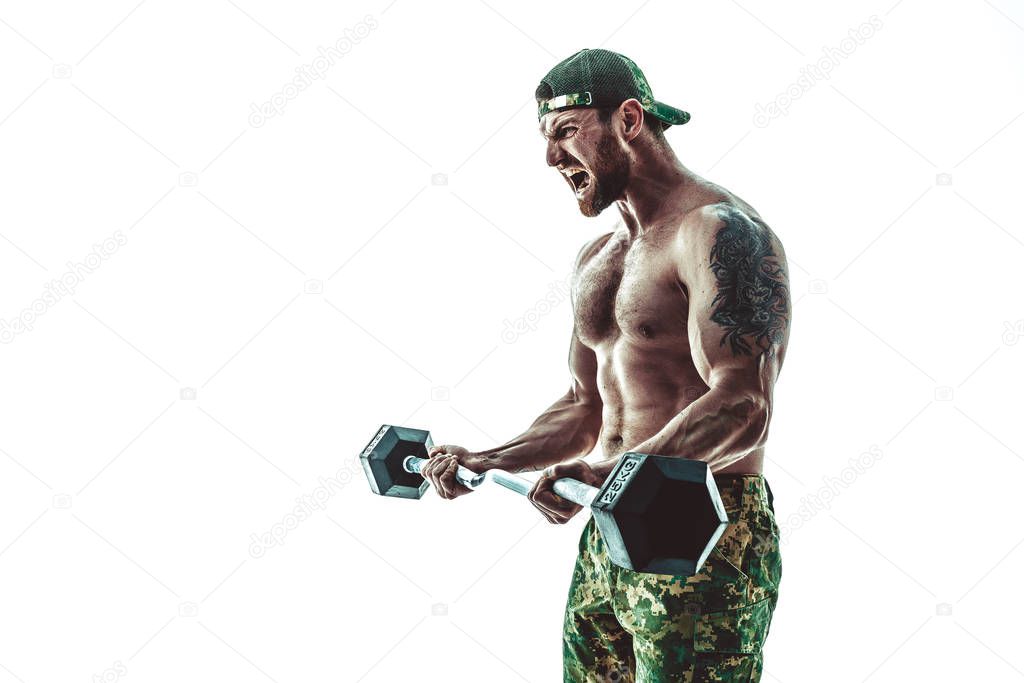 Muscular athlete bodybuilder man in camouflage pants with a naked torso workout with dumbbell on a white background.