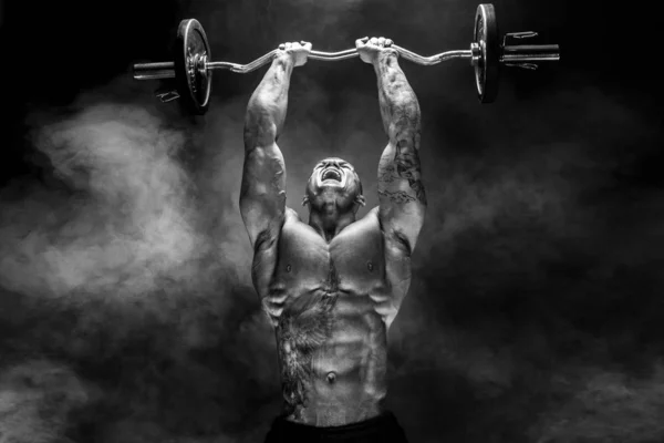 Сильный спортсмен поднимает тяжелый гантель в дыму — стоковое фото