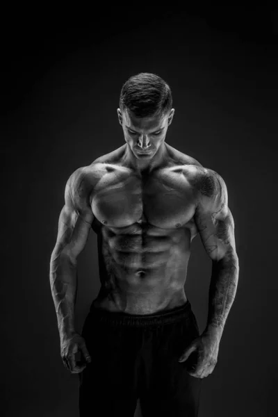 Bodybuilder poseren. Fitness gespierde man op donkere achtergrond. — Stockfoto