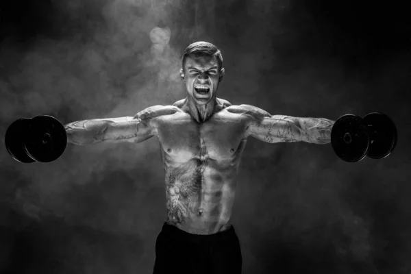 Strong sportsman lifting heavy dumbbell in smoke — Stock Photo, Image