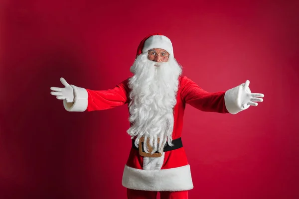 Homem bonito de meia idade vestindo traje de Papai Noel em pé sobre fundo vermelho isolado sorrindo alegre com os braços abertos como boas-vindas amigáveis, saudações positivas e confiantes — Fotografia de Stock