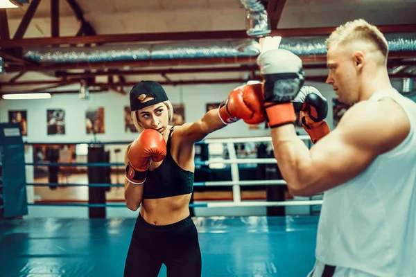 Mujer joven haciendo ejercicio con entrenador en la lección de boxeo y defensa personal — Foto de Stock