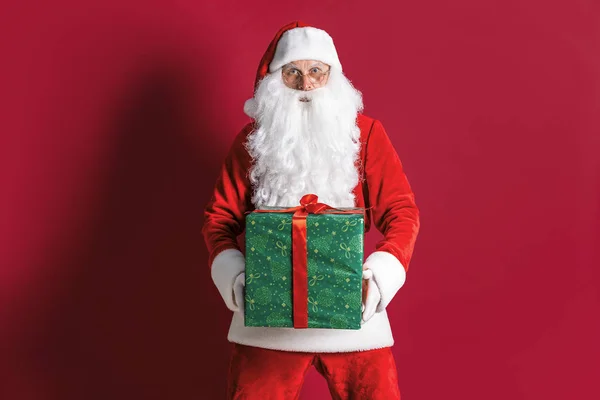 Фото доброго Санта-Клауса, дарящего рождественский подарок и смотрящего в камеру — стоковое фото