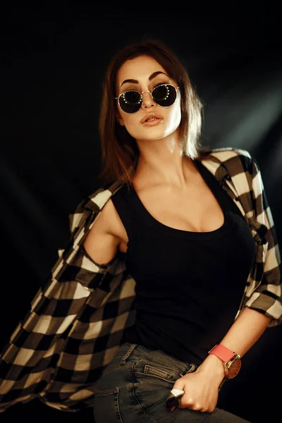 Menina em óculos e camisa xadrez em um fundo escuro — Fotografia de Stock