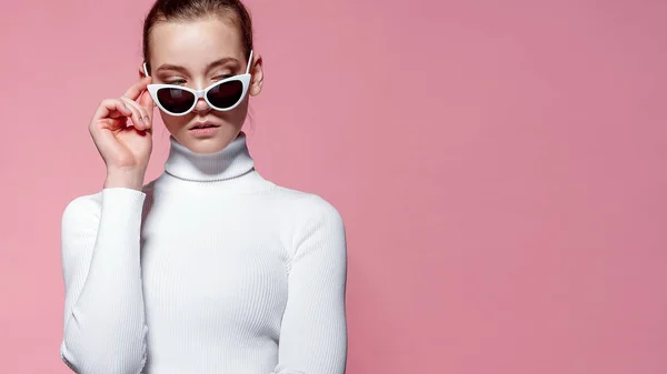 Fashion studio bild av vackra eleganta kvinnan i vit stickad golf och solglasögon poserar över rosa vägg — Stockfoto
