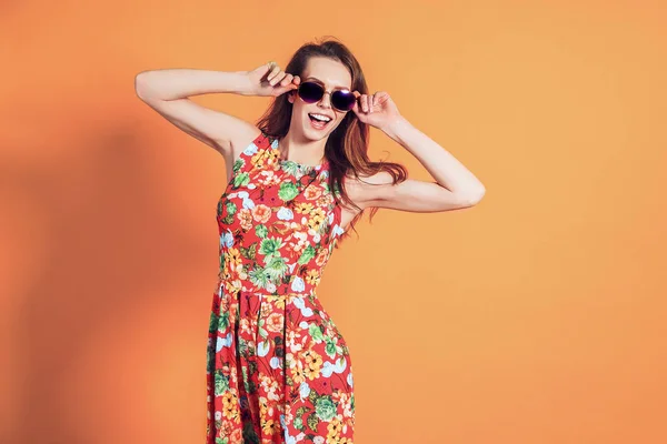 Meisje in bloemenjurk emotioneel poseert op de oranje achtergrond — Stockfoto