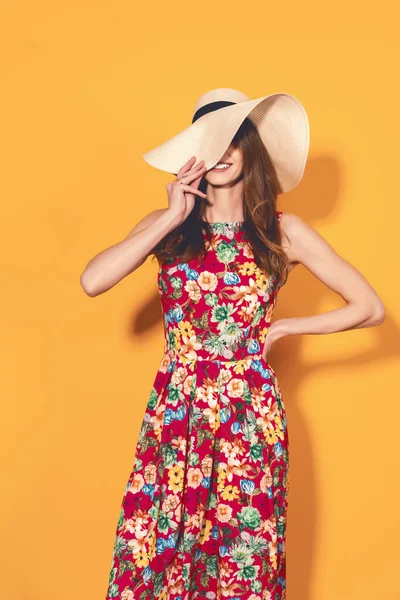 Menina em vestido floral e chapéu fechar metade de seu rosto e emocionalmente posa no fundo amarelo — Fotografia de Stock