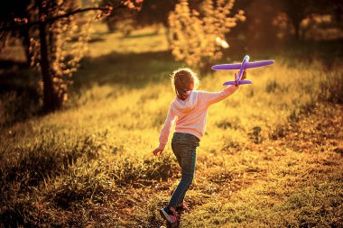 Küçük kız parkın dışındaki havaya oyuncak bir uçak fırlatıyor. Çocuk oyuncak bir uçak fırlatıyor. Güzel küçük kız çimlerin üzerinde durur ve pembe oyuncak bir uçak fırlatır.