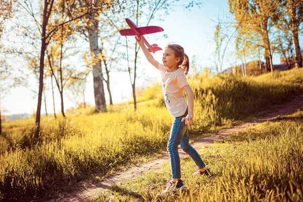 Niña lanza un avión de juguete al aire libre en el parque. Niño lanza un avión de juguete. Hermosa niña se para en la hierba y lanza un avión de juguete rosa — Foto de Stock