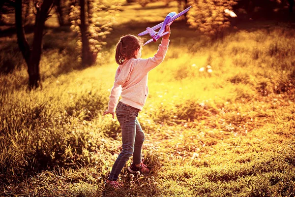 Niña lanza un avión de juguete al aire libre en el parque. Niño lanza un avión de juguete. Hermosa niña se para en la hierba y lanza un avión de juguete rosa — Foto de Stock