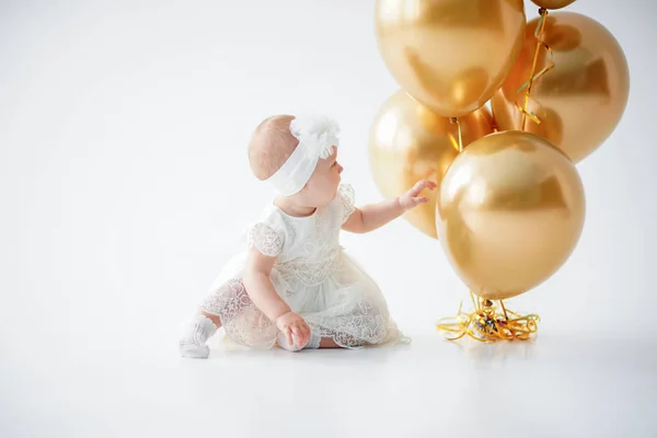 Uma menina de um ano sentada com um monte de balões dourados . — Fotografia de Stock