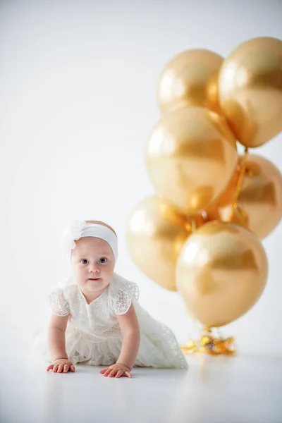 Une petite fille d'un an assise avec un tas de ballons dorés . — Photo